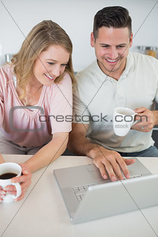 Couple using laptop while holding coffee cups