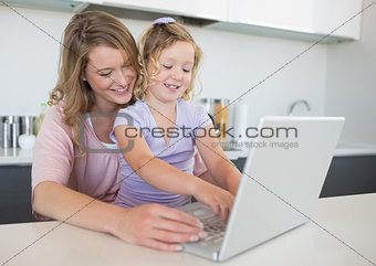 Mother assisting daughter in using laptop at table