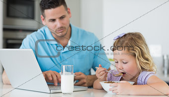 Father looking at daughter having breakfast
