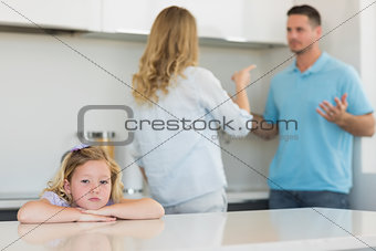 Sad girl leaning on table while parents arguing
