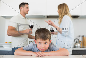 Sad boy leaning on table while parents arguing