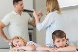 Children leaning on table while parents arguing