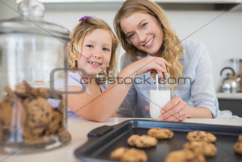 Mother with girl dipping cookie in milk