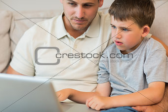 Father and son using laptop on sofa