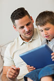 Father and son using tablet computer on sofa