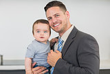 Smart businessman carrying baby boy in kitchen