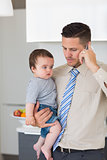 Businessman carrying baby boy while using mobile phone