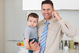 Businessman carrying baby while while using cellphone