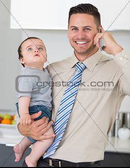 Businessman using cellphone while carrying baby in house