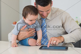 Businessman using tablet while holding baby