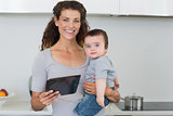 Mother carrying baby boy while holding digital tablet