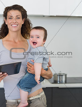 Mother with tablet computer carrying cheerful baby