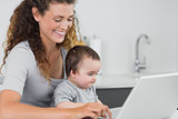 Smiling woman with baby using laptop