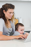 Woman with baby using laptop at counter