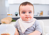 Messy baby eating food in kitchen