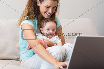 Mother using laptop while holding baby