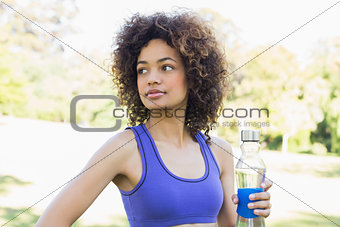 Thoughtful sporty woman holding water bottle