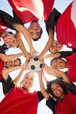 Soccer team with ball forming huddle against sky