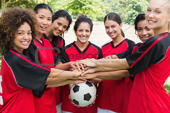Confident soccer team stacking hands on ball