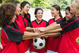 Excited soccer team stacking hands on ball