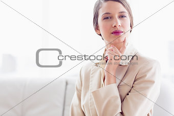 Young thinking businesswoman sitting on sofa looking at camera