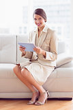 Happy businesswoman sitting on sofa using tablet pc