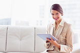 Stylish businesswoman sitting on sofa using tablet smiling at camera