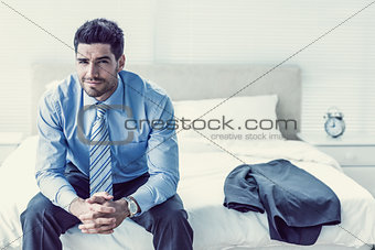 Handsome businessman sitting on bed looking at camera