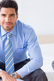 Businessman sitting on bed smiling at camera