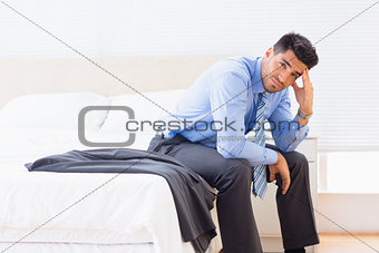 Frowning businessman sitting at edge of bed looking at camera