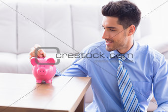 Smiling businessman putting coins into piggy bank