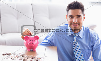 Cheerful businessman putting coins into piggy bank