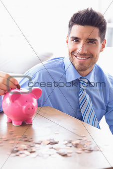 Handsome businessman putting coins into piggy bank looking at camera