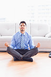 Handsome businessman meditating in lotus pose on the floor