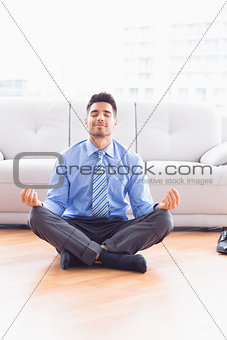 Handsome businessman meditating in lotus pose on the floor
