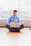 Businessman sitting on floor using his laptop smiling at camera