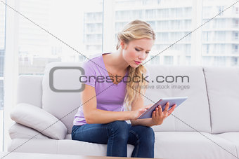 Beautiful blonde sitting on her sofa using her tablet pc