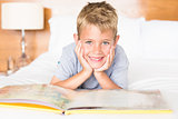 Smiling blonde boy lying on bed reading a storybook