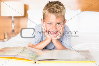 Smiling blonde boy lying on bed reading a storybook