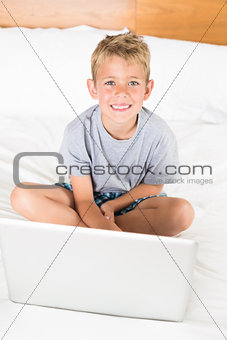 Cute blonde boy sitting on bed using laptop