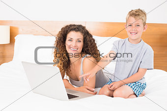 Happy blonde boy and mother on bed using laptop