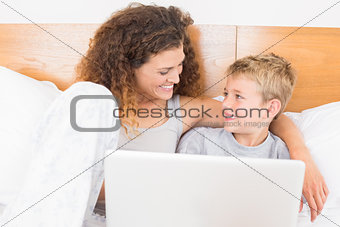 Smiling mother and son sitting on bed using laptop