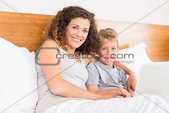 Smiling mother and son sitting on bed with laptop