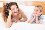 Happy mother and son lying on bed looking at camera