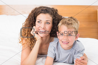 Happy mother and son lying on bed looking away