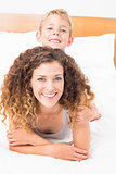 Cheerful mother and son posing on bed looking at camera