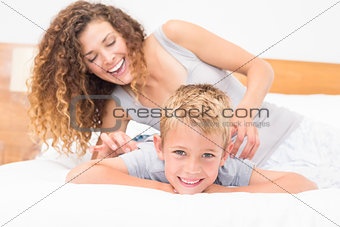Happy mother tickling her cute son on bed