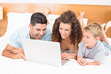 Happy family using laptop together on bed