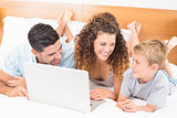 Smiling family using laptop together on bed