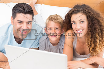 Happy young family using laptop together on bed